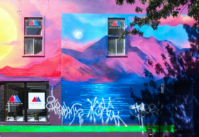 on the side of a building, part of Izabelle Duguay's “Toucher L'horizon” with its pink/blue mountain rising above the blue water