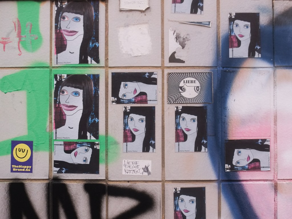 urban art, street art, in Cologne Germany, near Ehrenfeld station, arrangement of stickers with woman's portrait, all byHenry Paulson, all rather similar black hair and blue eyes,