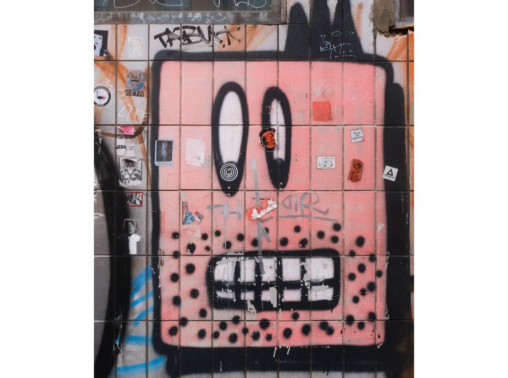 urban art, street art, in Cologne Germany, near Ehrenfeld station, pink rectangle, face with oval slitty eyes and rectangular mouth, black dots on cheeks and chin