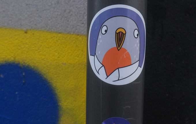 urban art, street art, in Cologne Germany, near Ehrenfeld station, sticker with a pigeon head, yellow beak, wearing a white shirt with a collar