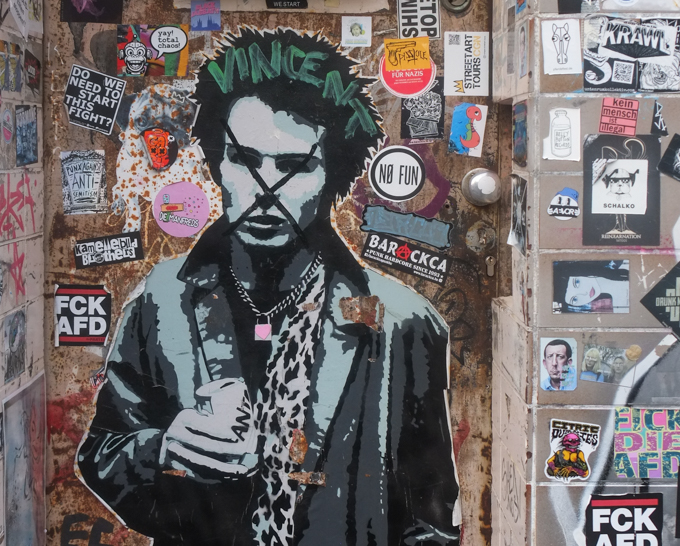 urban art, street art, in Cologne Germany, near Ehrenfeld station, black and white stencil, large, of Sid vicious from punk rock band Sex Pistols. he is holding a can of Fanta pop. other small slap graffiti around him