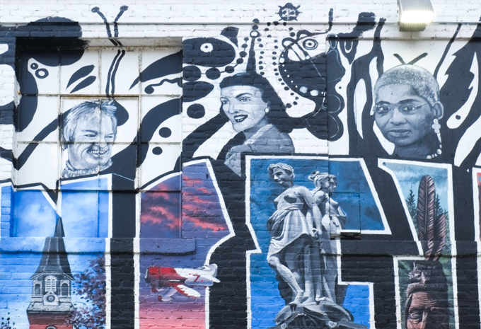 part of a mural in Springfield Massachusetts, with word Springfield in capital letters and in colour, with illustrations inside the letters and black and white images of people and things associated with the city. Heads or portraits along the top of the name of the city, a steeple, a red and white airplane, a statue of two topless women, a feather in an Inndian headdrress