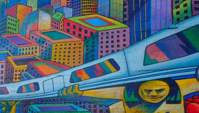 part of a mural at 24th street Bart station, a train is running on elevated tracks that are held up by men, faceless red people wait under the tracks, colourful city buildings in the background, originally painted in 1975 by Michael Rios, Richard Montes and Tony Machado, and updated in 2026