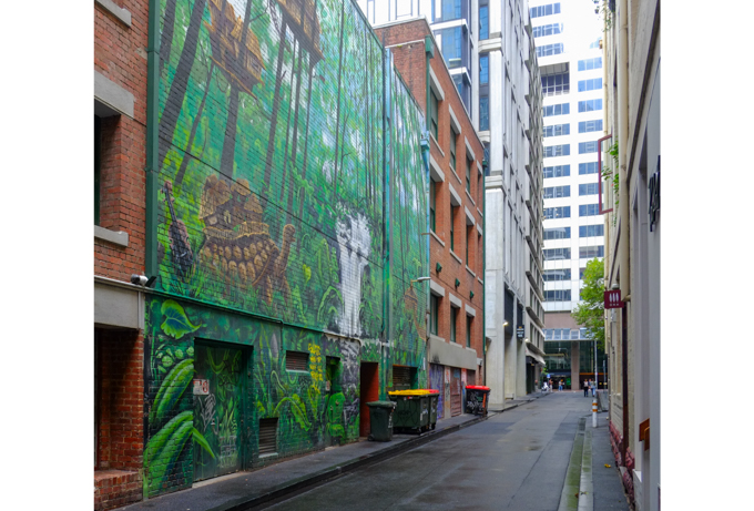 Gallaghers Place in Melbourne, an alley with tall buildings on both sides, murals by Mike Makatron and Conrad Bizjak on one of the walls.