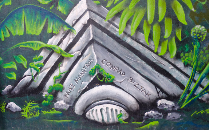 broken top of a grey stone column in a mural with names of the artists on it, Mike Makatron and Conrad Bizjak