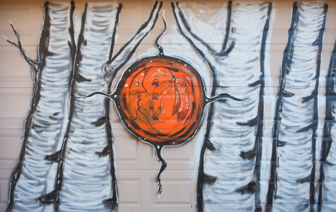 street art mural, birch trees, with orange circle in the middle, faces in the circle, feathers too