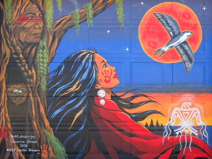 mural by Veronica Orozco, woman sitting against tree trunk while looking out over a lake, swallow flying past, against a setting sun, or it could be the moon, red handprint on woman's cheek, bird nest in tree, stars in sky