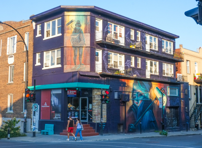 building with two murals, on upper floor is a woman with a paint roller, by SNIKR, lower floor has portrait of the young woman with a paint roller as well