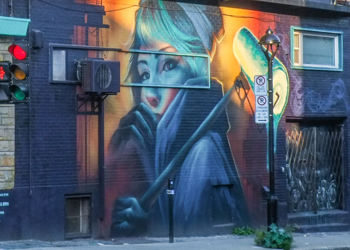 building with two murals bySNIKR, mural on the lower level seen closer. young woman with large collar on her jacket, paint roller over her shoulder