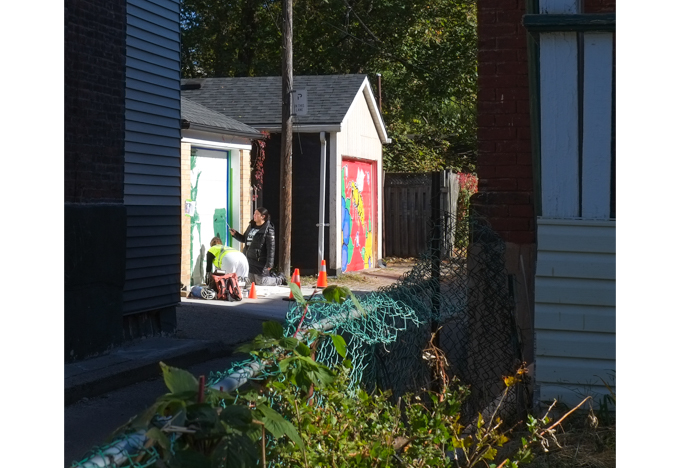 two women painting a street art mural on a garage door in Miriam Garfinkle Lane