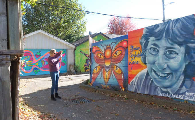woman taking pictures of street art murals on garage doors in Miriam Garfinkle Lane,