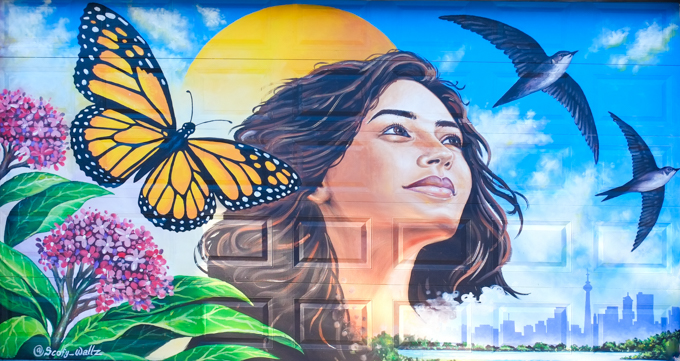 street art mural on garage door in Miriam Garfinkle Lane, by Scofy Wallz, woman's portrait, Toronto skyline with lake and CN tower, birds, butterfly, milkweed