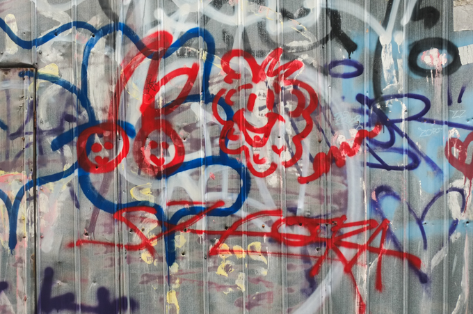 scrawl graffiti in blue and red including a couple of happy faces on corrugated metal fence