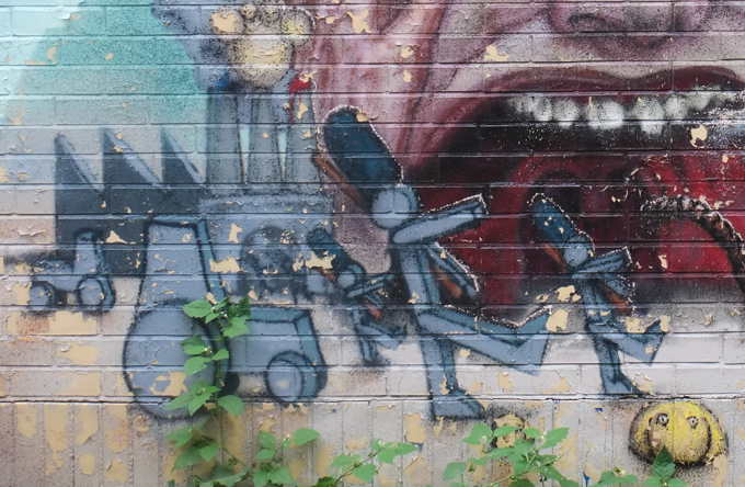 mural by scribe, large face with blood shot blue eyes, wide open red screaming mouth ith teeth, and little characters in front, some faceless ones marching