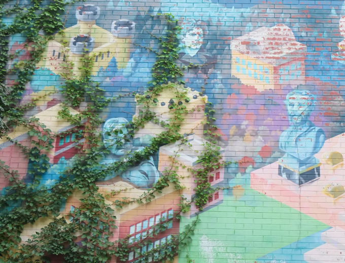 weeds and vines in real life are growing over part of a mural painted by Mylène Chabot, Marie Gosselin, Benjamin Picard, and Mathias Vouters