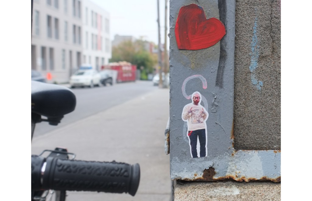 two pieces of graffiti on a wall, one is a tiny man and the other is a red heart