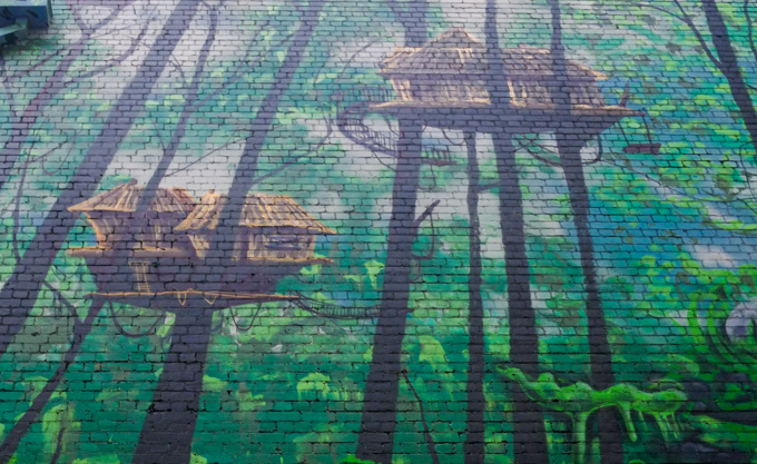 urban art mural, houses built high up in the trees, connected by rope bridges and ladders