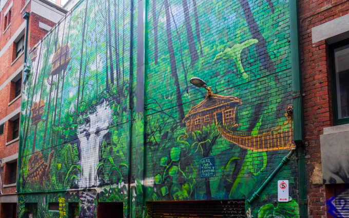 Part of a mural in Gallaghers Place in Melbourne, by Mike Makatron and Conrad Bizjak, There are houses up high in the trees, a waterfall, and a large turtle