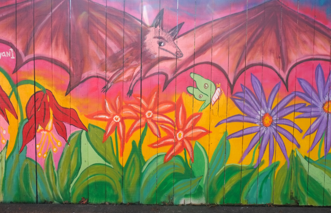 street art mural on garage door in Miriam Garfinkle Lane, by Trina Moyan, a large bat flies over a garden