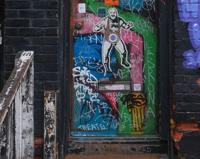 doorway covered with graffiti including a bald wrestler on the door wearing bootss